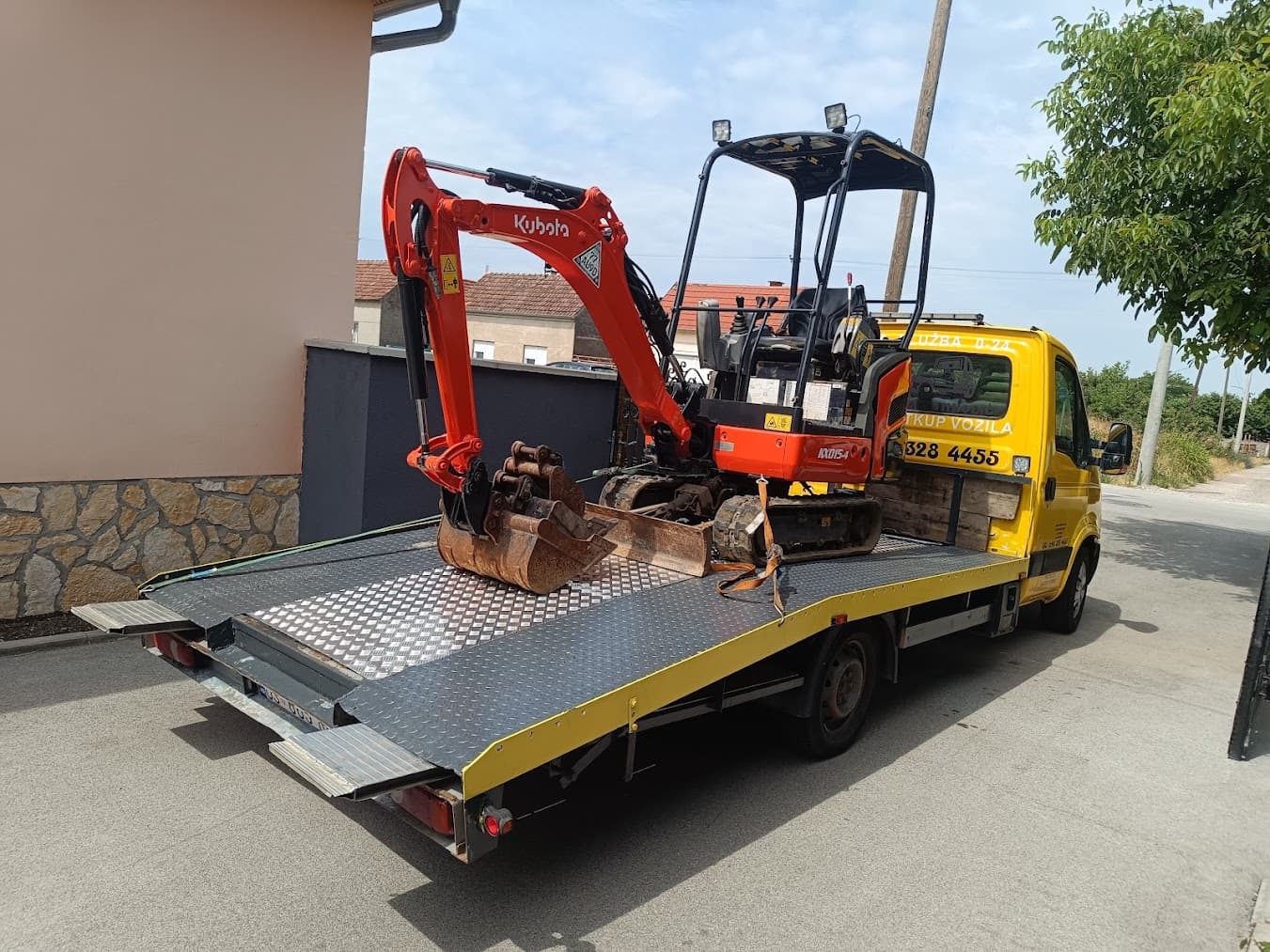 Narančasti Kubota mini bager utovaren na platformi vučnog vozila