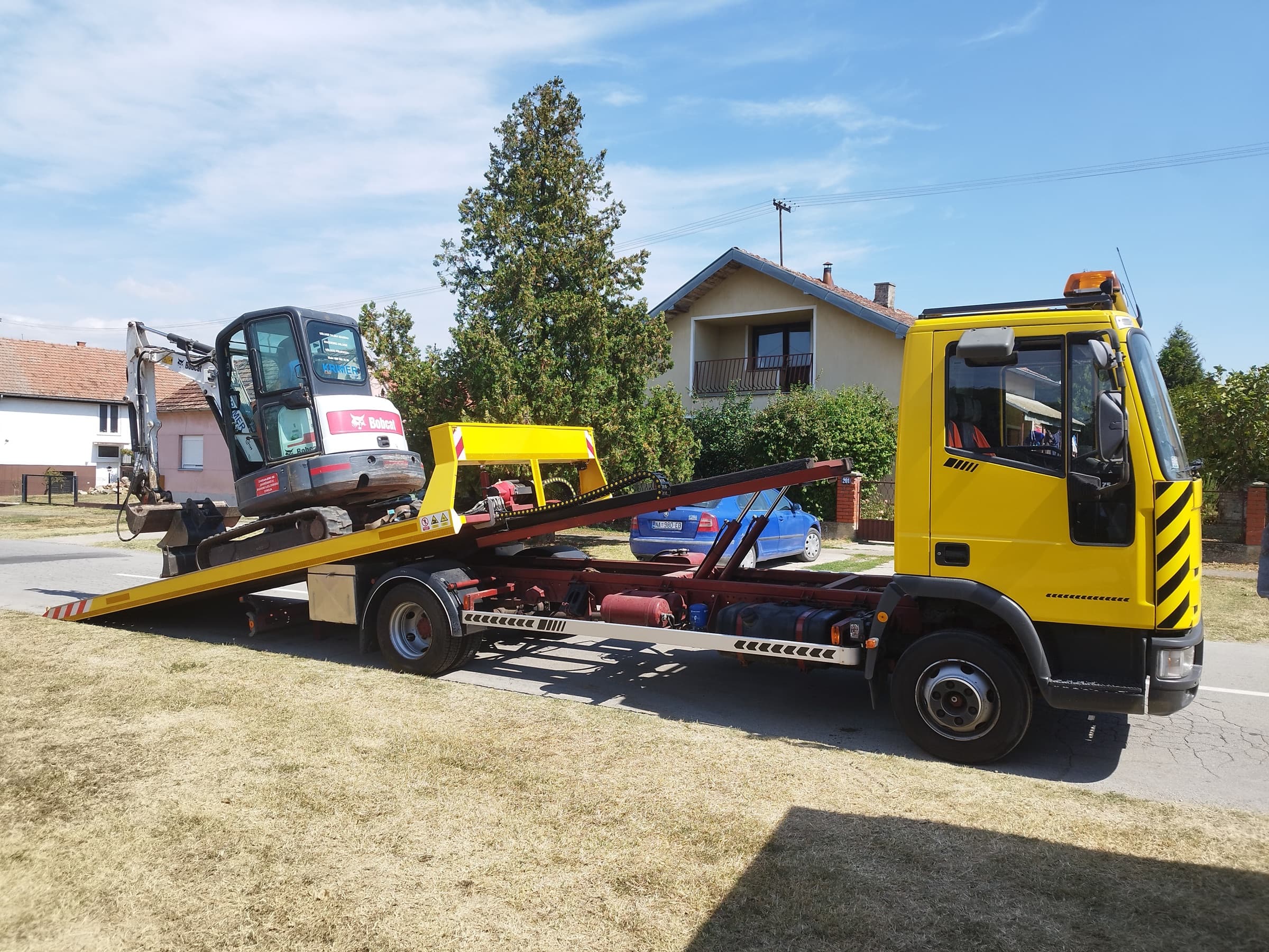Bobcat mini bager na nagnutoj platformi tijekom utovara