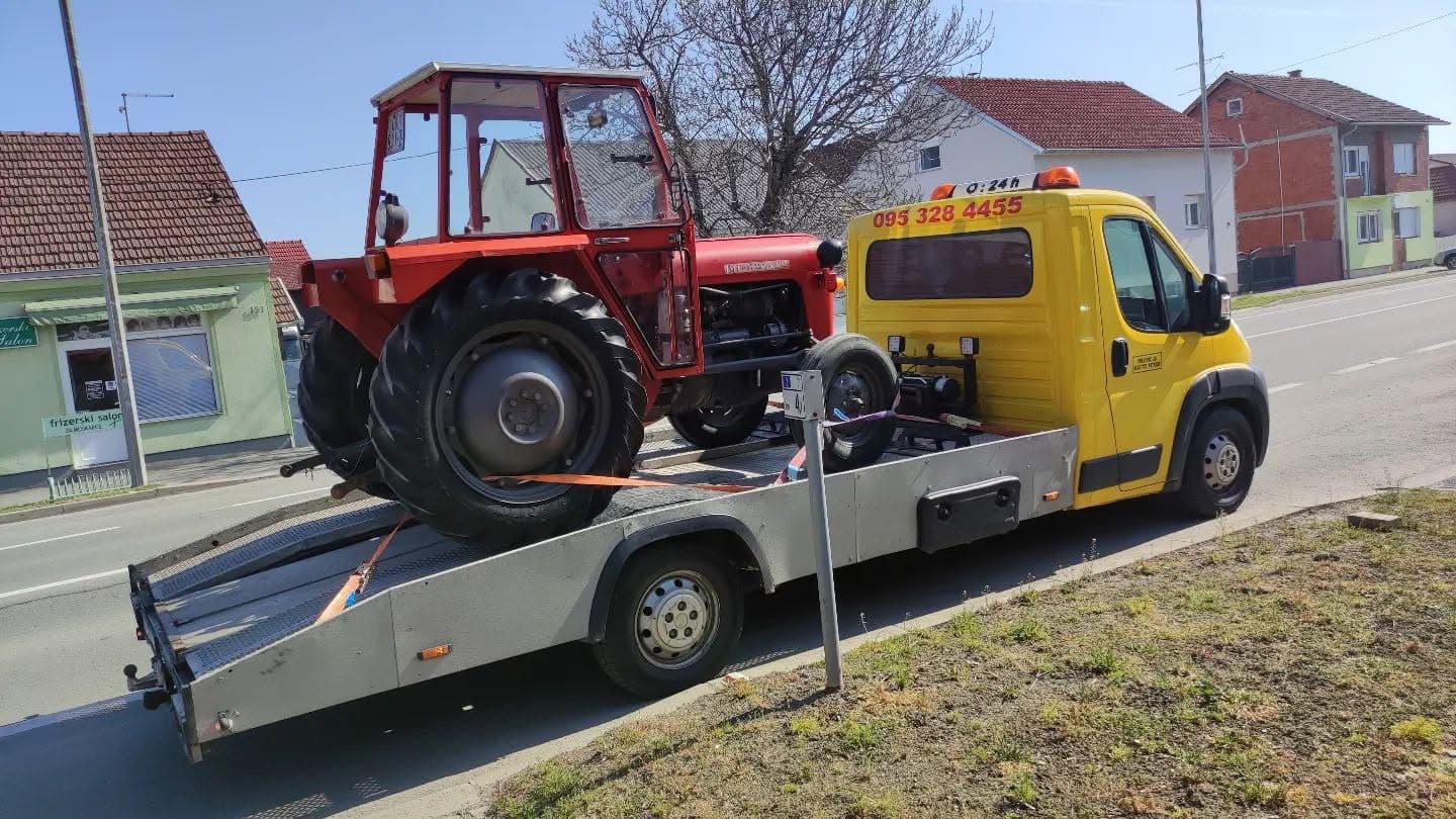Crveni traktor utovaren na platformi vučnog vozila Nikolić